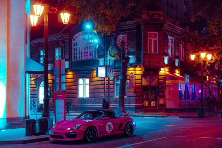 Nighttime street in downtown Yerevan with a pink convertible parked under neon lights.