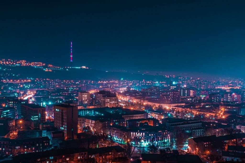 Panoramic night view of Yerevan’s illuminated cityscape with the Yerevan TV Tower glowing atop the hill in the background.