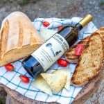A bottle of Georgian natural wine with fresh bread, cheese, and cherry tomatoes.