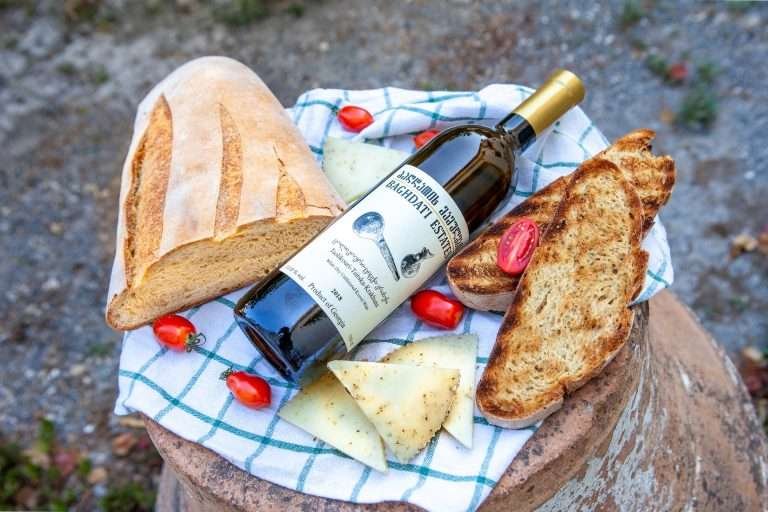 A bottle of Georgian natural wine with fresh bread, cheese, and cherry tomatoes.
