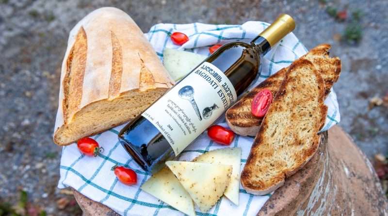 A bottle of Georgian natural wine with fresh bread, cheese, and cherry tomatoes.