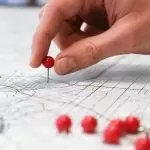 Hand placing a red pin on a detailed city map with multiple red pins.
