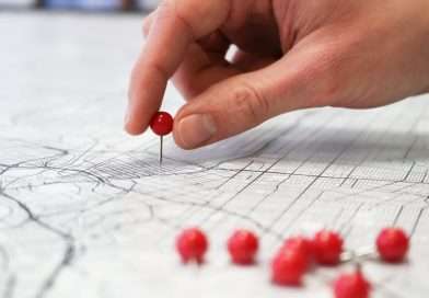 Hand placing a red pin on a detailed city map with multiple red pins.