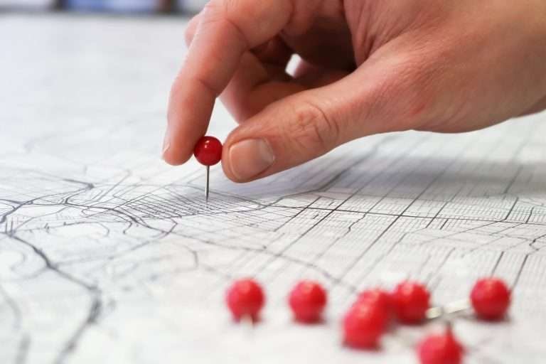 Hand placing a red pin on a detailed city map with multiple red pins.