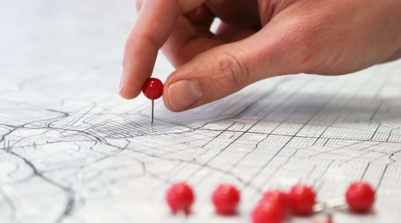 Hand placing a red pin on a detailed city map with multiple red pins.