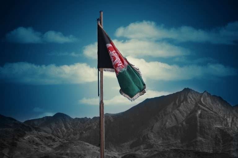Tattered Afghan flag waving before mountainous landscape under a blue sky