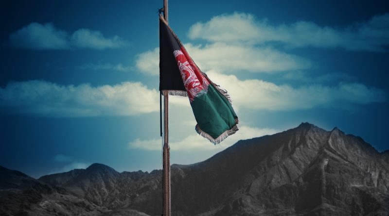 Tattered Afghan flag waving before mountainous landscape under a blue sky