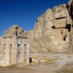 Naqsh-e Rustam necropolis showing the white Kaaba-ye Zartosht tower in the foreground and an Achaemenid cliff-tomb façade carved into the limestone cliff at Fars Province, Iran.
