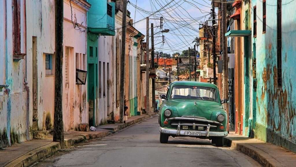 Vintage green car driving down a pastel-painted street in Cuba’s historic town.