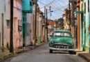 Vintage green car driving down a pastel-painted street in Cuba’s historic town.