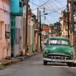 Vintage green car driving down a pastel-painted street in Cuba’s historic town.