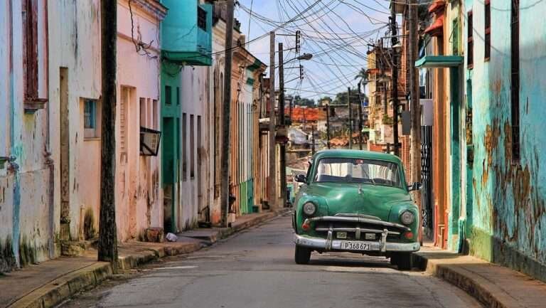 Vintage green car driving down a pastel-painted street in Cuba’s historic town.