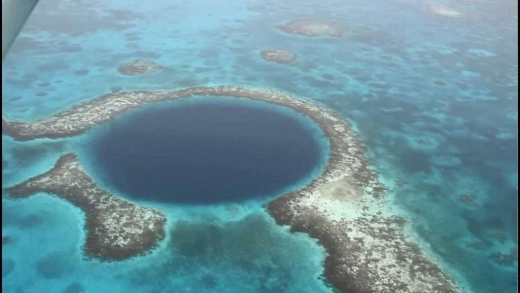 Aerial view of a circular coral atoll ring enclosing a deep blue lagoon in turquoise ocean waters