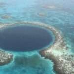Aerial view of a circular coral atoll ring enclosing a deep blue lagoon in turquoise ocean waters