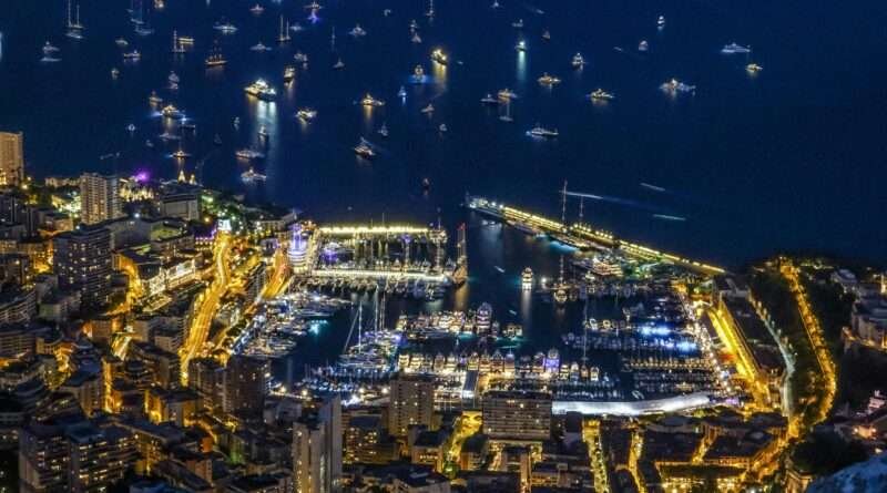 Aerial nighttime view of Monaco’s Port Hercule on the French Riviera, with luxury yachts docked amid shimmering city lights.