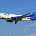 Nauru Airlines Boeing 737-300 aircraft in white, blue, and yellow livery descending against a clear blue sky.