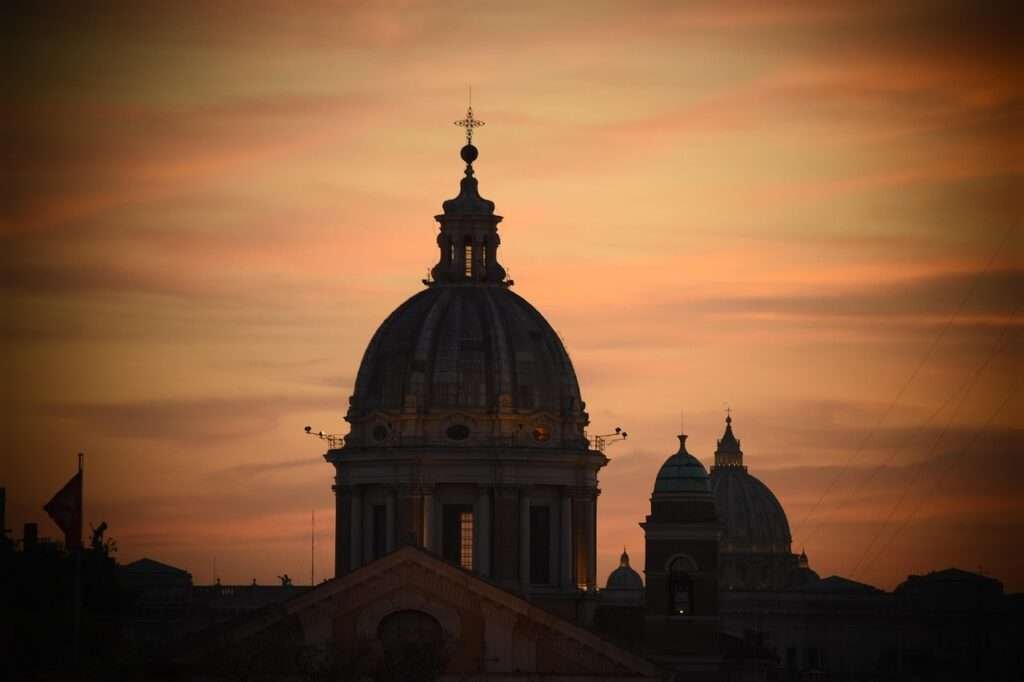 Silhouette of St. Peter’s Basilica dome against a vivid sunset sky in Vatican City