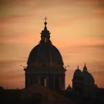 Silhouette of St. Peter’s Basilica dome against a vivid sunset sky in Vatican City