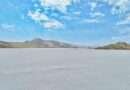 Panoramic view of Oksukon Lake’s white salt flat with distant mountains under a bright sky