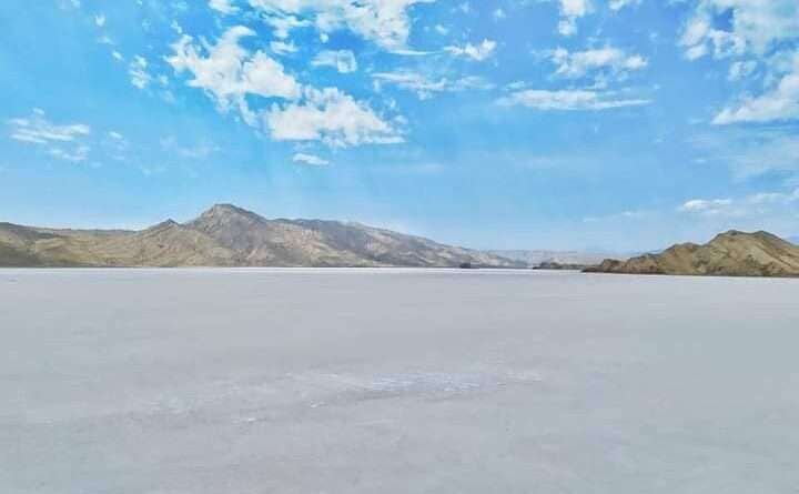 Panoramic view of Oksukon Lake’s white salt flat with distant mountains under a bright sky