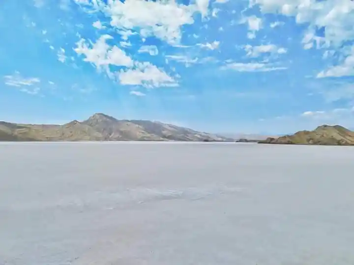 Panoramic view of Oksukon Lake’s white salt flat with distant mountains under a bright sky