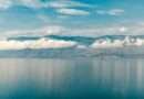 Wide-angle view of Lake Tanganyika’s deep blue waters reflecting a ribbon of white clouds, with the rugged mountains of the East African Rift rising along the distant shoreline under a partly cloudy sky.