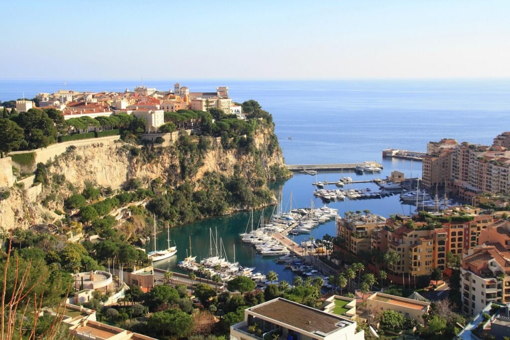 Monaco-Ville on the Rock of Monaco overlooking Fontvieille Marina and the Mediterranean Sea, with yachts, terracotta rooftops, and steep coastal cliffs on a clear day