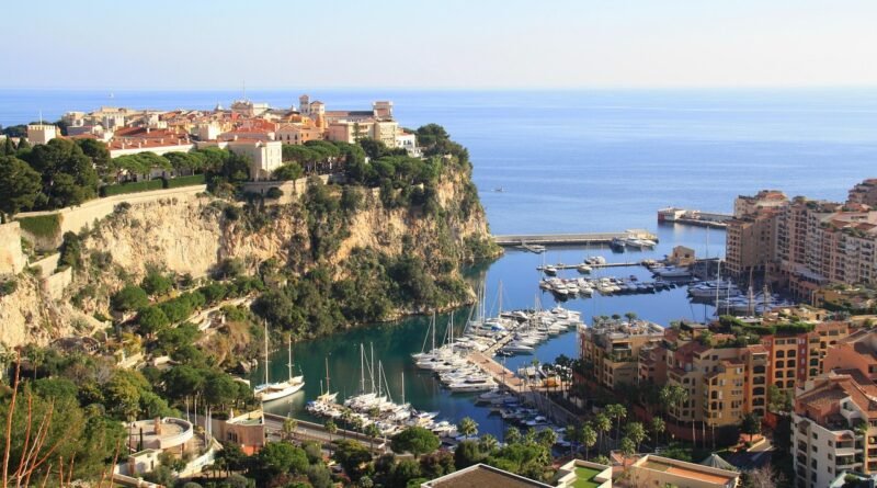 Monaco-Ville on the Rock of Monaco overlooking Fontvieille Marina and the Mediterranean Sea, with yachts, terracotta rooftops, and steep coastal cliffs on a clear day