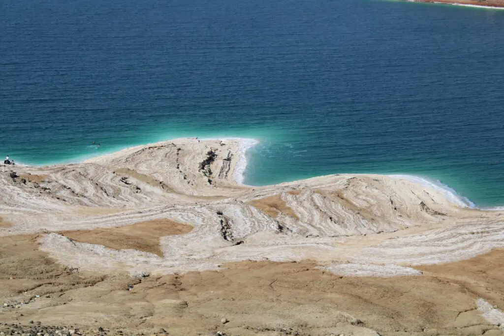 Salt-crusted shoreline of the Dead Sea with turquoise water and mineral layers visible.
