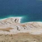 Salt-crusted shoreline of the Dead Sea with turquoise water and mineral layers visible.