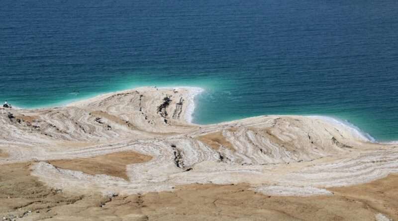 Salt-crusted shoreline of the Dead Sea with turquoise water and mineral layers visible.