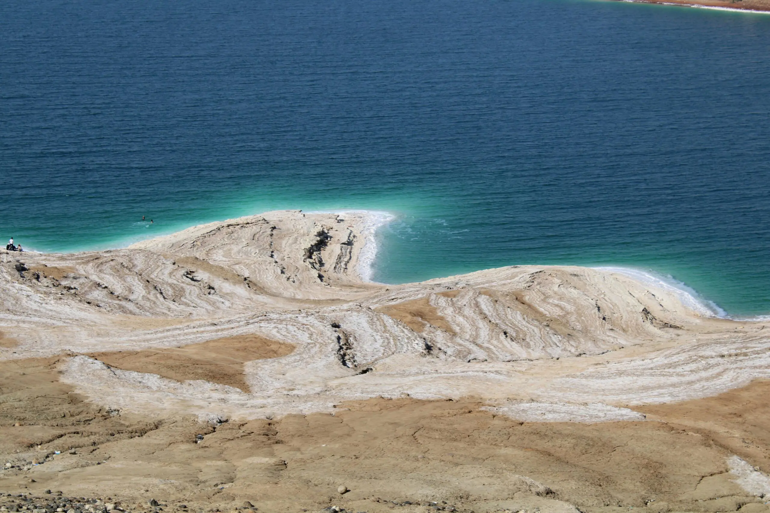 Salt-crusted shoreline of the Dead Sea with turquoise water and mineral layers visible.