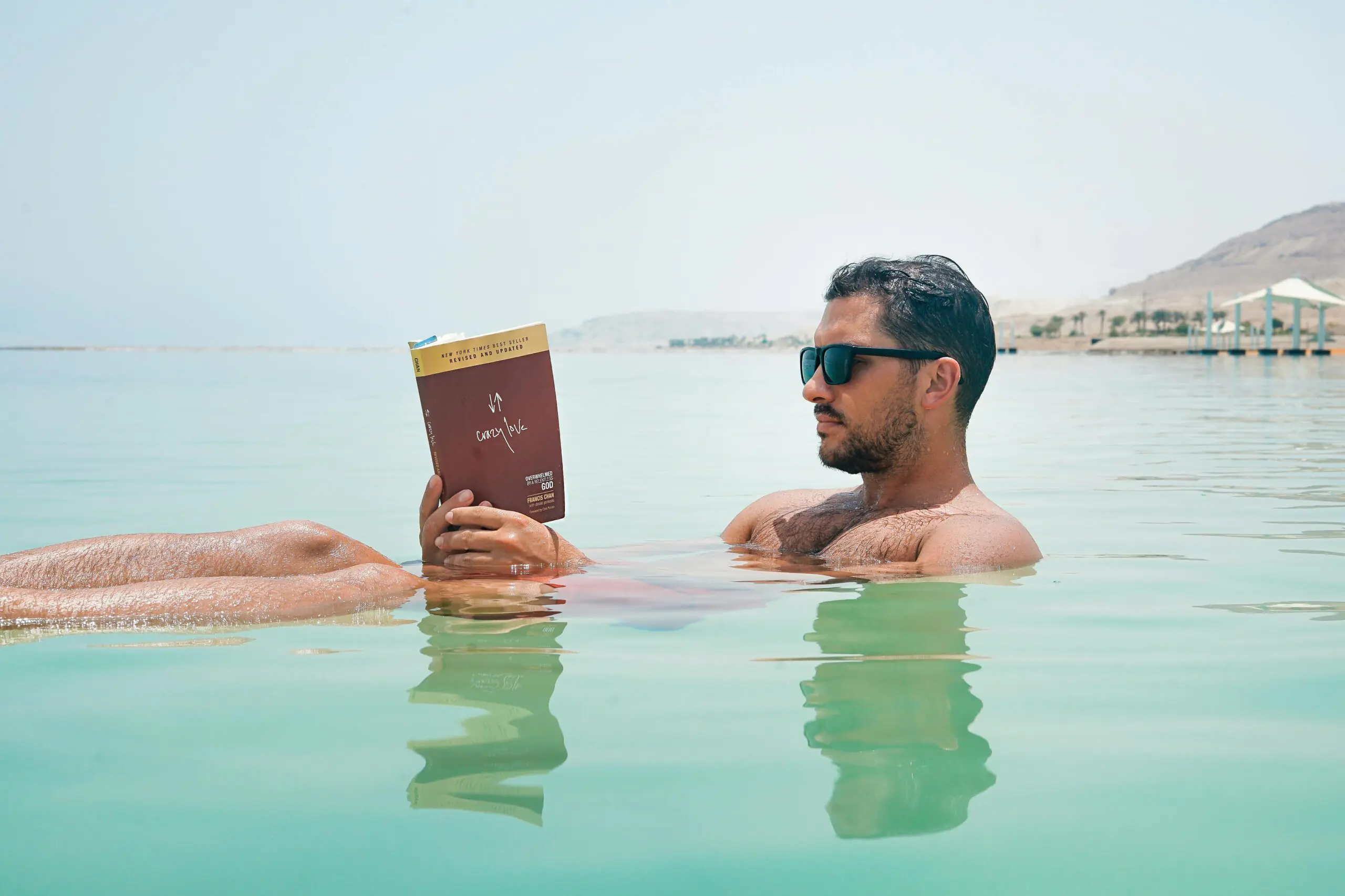 Man floating and reading a book in the Dead Sea, Israel, demonstrating effortless buoyancy in hypersaline water