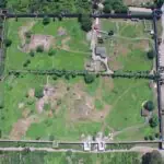 Aerial photograph of Gonio Fortress showing its rectangular stone walls, towers, and excavated interior structures surrounded by greenery.