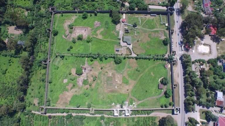 Aerial photograph of Gonio Fortress showing its rectangular stone walls, towers, and excavated interior structures surrounded by greenery.