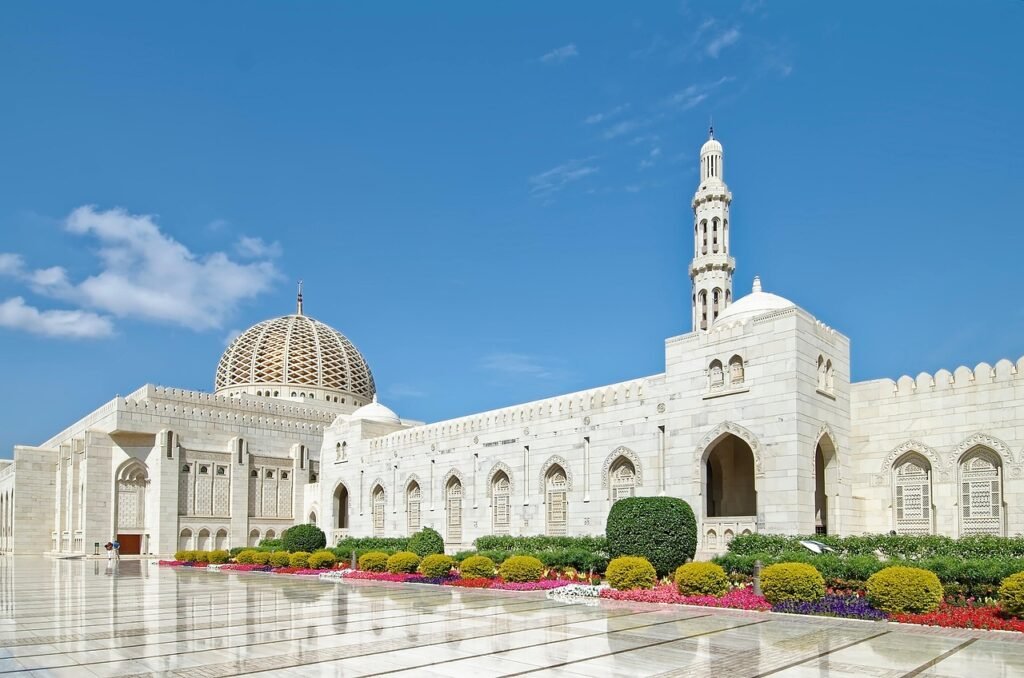 Sultan Qaboos Grand Mosque in Muscat, Oman with white marble architecture under blue sky