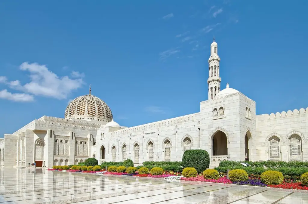 Sultan Qaboos Grand Mosque in Muscat, Oman with white marble architecture under blue sky