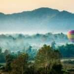 Colorful hot air balloon floating over misty fields and limestone mountains in Vang Vieng, Laos