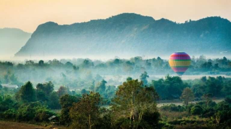 Colorful hot air balloon floating over misty fields and limestone mountains in Vang Vieng, Laos