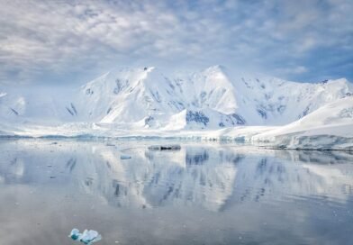 Snow-covered Antarctic mountains and coastal glaciers reflected in calm Southern Ocean waters on the Antarctic Peninsula.