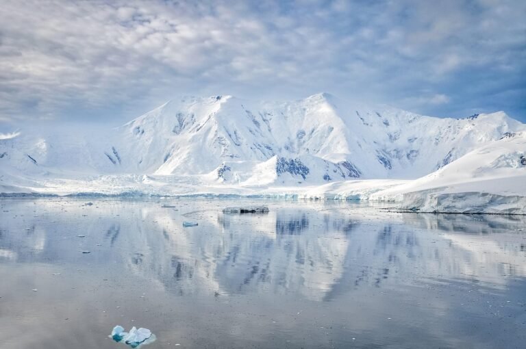 Snow-covered Antarctic mountains and coastal glaciers reflected in calm Southern Ocean waters on the Antarctic Peninsula.