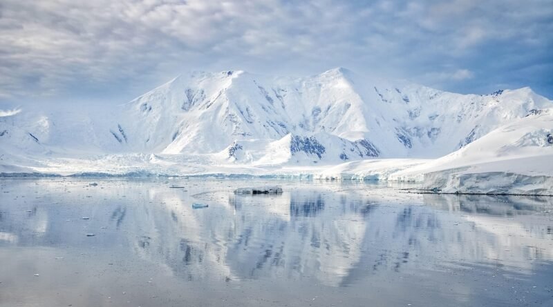 Snow-covered Antarctic mountains and coastal glaciers reflected in calm Southern Ocean waters on the Antarctic Peninsula.