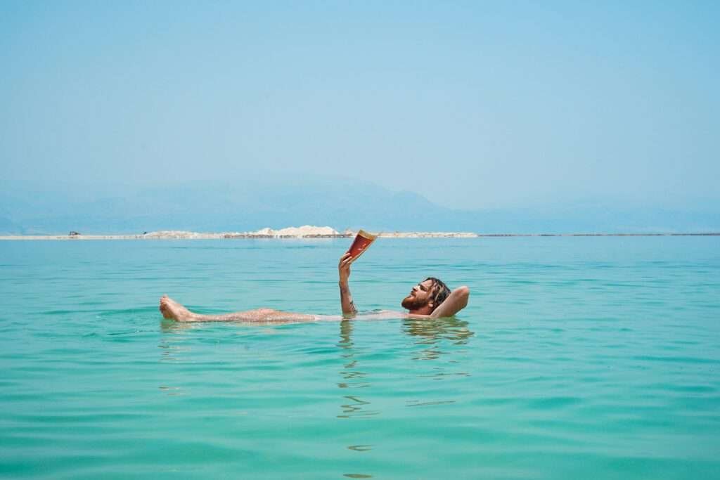 Man floating on his back in the Dead Sea while reading a book, demonstrating natural buoyancy in hypersaline water