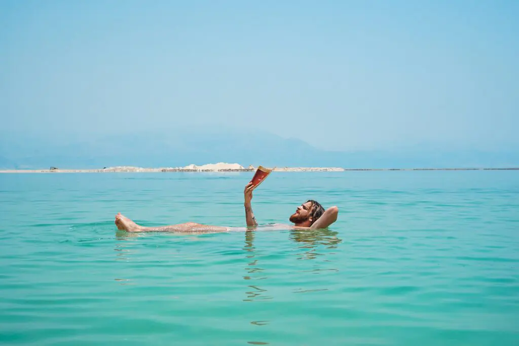 Man floating on his back in the Dead Sea while reading a book, demonstrating natural buoyancy in hypersaline water