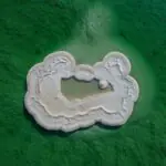 Aerial view of a white salt island formation in the green waters of the Dead Sea, showing crystallized magnesium and mineral deposits.