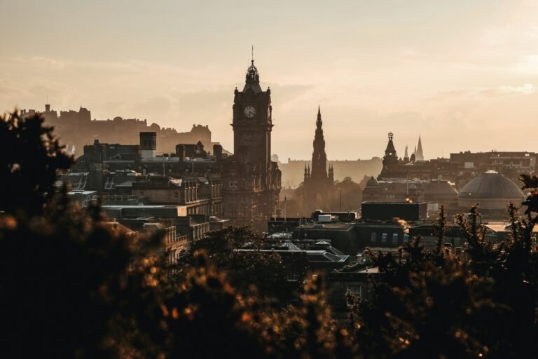Sunset skyline of Edinburgh, Scotland, with the Balmoral Clock Tower, the gothic Scott Monument, and Edinburgh Castle rising above Old and New Town rooftops.