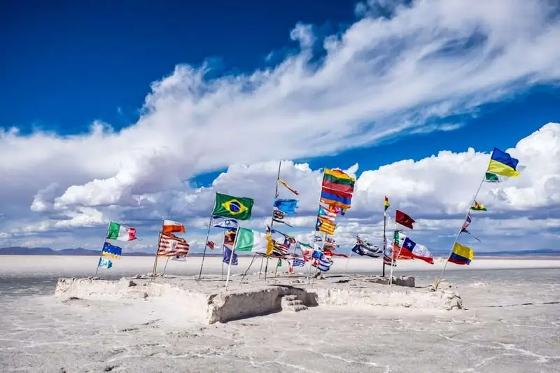 Flags of different countries flying together on a salt flat under a blue sky