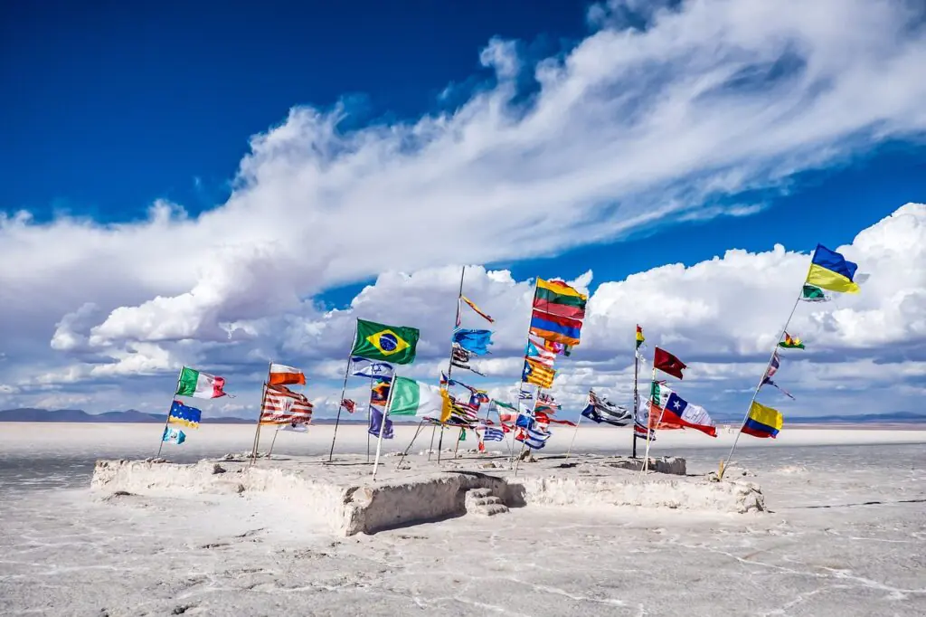 Flags of different countries flying together on a salt flat under a blue sky