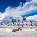 Flags of different countries flying together on a salt flat under a blue sky