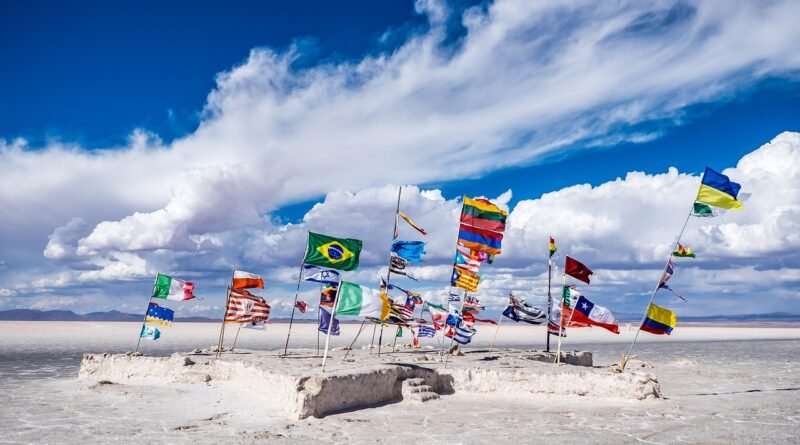 Flags of different countries flying together on a salt flat under a blue sky